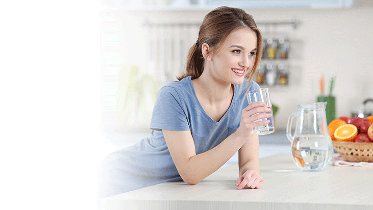 Smiling woman drinking water over a kitchen counter.