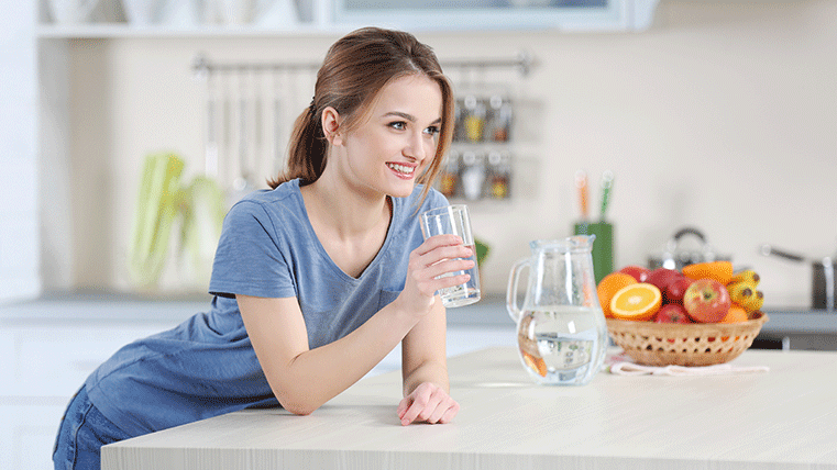 Smiling woman drinking water over a kitchen counter.